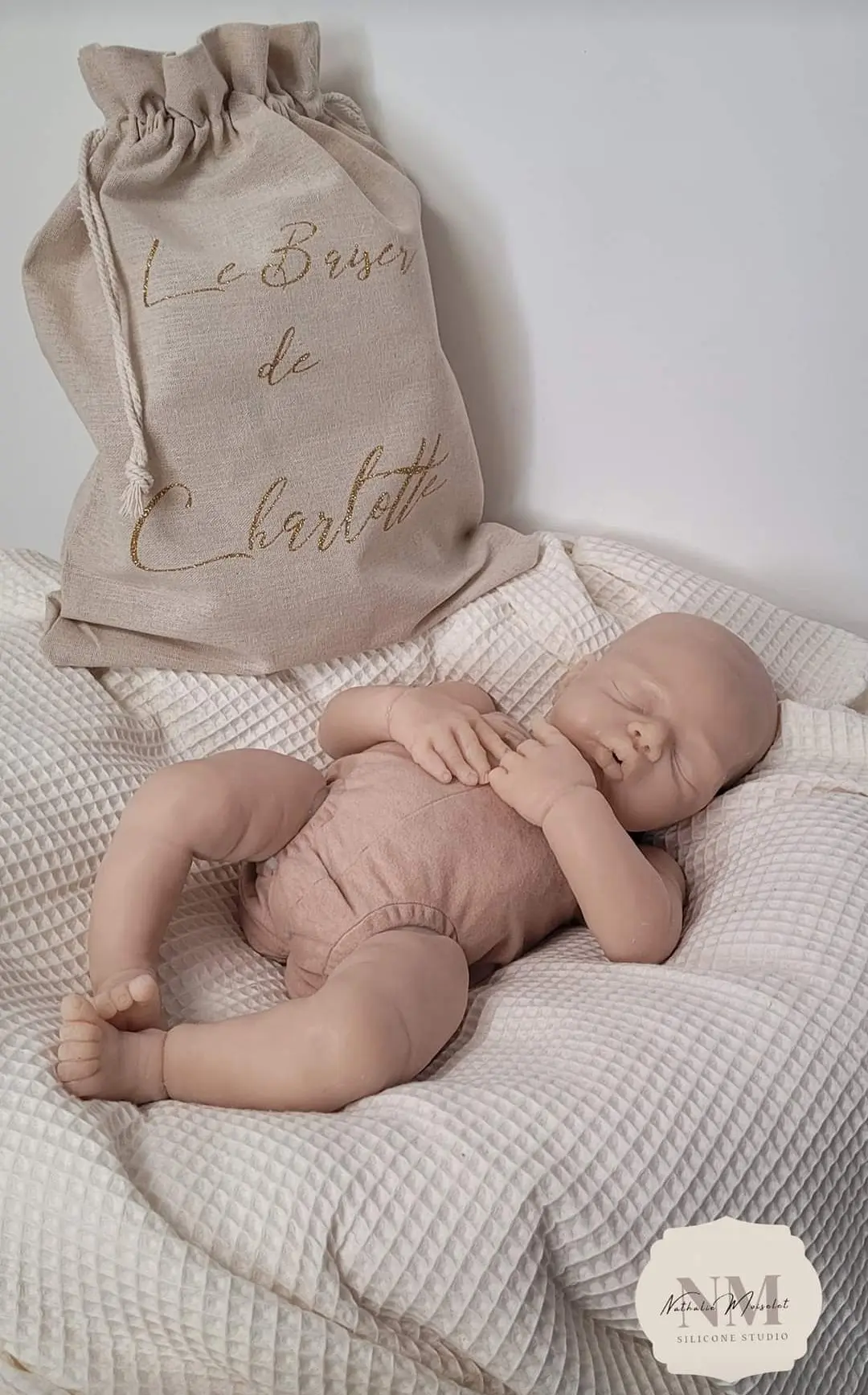 Photo d'un bébé reborn en silicone allongé sur un couvant.